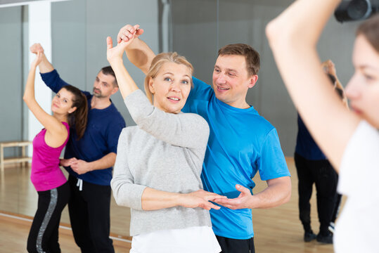 Attractive mature blonde dancing slow ballroom dance in pair during group training in dance hall