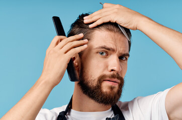 professional hairdresser man in gray apron doing his hair on blue background and cropped view