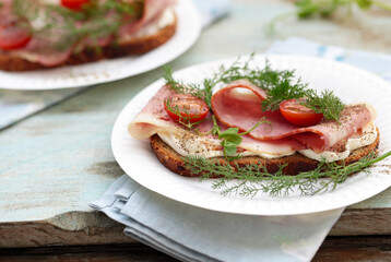 sanduíches abertos no café da manhã, compostos por pão de cereal, queijo Philadelphia, bacon defumado, tomate cereja e verduras. 