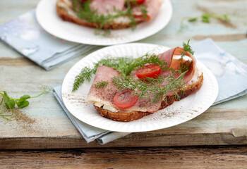 sanduíches abertos no café da manhã, compostos por pão de cereal, queijo Philadelphia, bacon defumado, tomate cereja e verduras. 