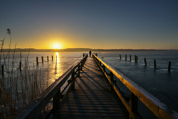 Sunrise over a frozen lake and a young woman as silhouette on the end of a long wooden jetty enjoying the landscape scenery, copy space,