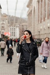 beautiful young woman drinks coffee from paper cup on city street. High quality photo