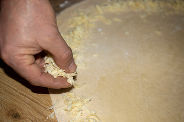 The hands of the cook who put grated cheese on the dough he rolls.