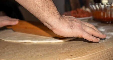 The hands of the cook who put grated cheese on the dough he rolls.