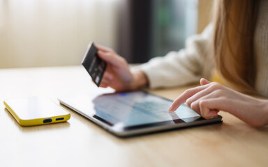 Fototapeta premium The girl makes a payment with a bank card on the Internet on a tablet. Close-up. Selective focus on the hand near the tablet display.