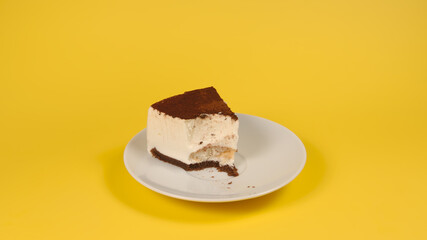 Bitten off piece of cake on a white dish on yellow background, isolated