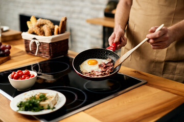 Close-up of man preparing friend eggs with bacon in the kitchen.