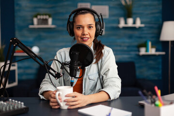 Fototapeta na wymiar Vlogger messaging her audience while making podcast in home studio for social media. Blogger recording online talk show using headphones, professional microphone looking at camera during broadcast.