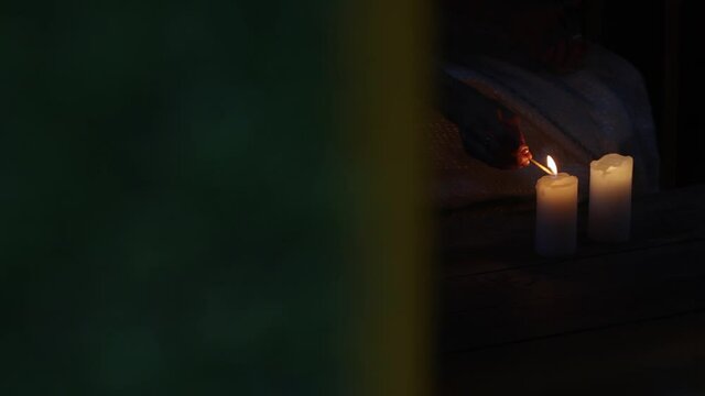 Burning candles. A woman's hand lights a candle from a match. The camera shoots through the window. Horizontal panorama.
