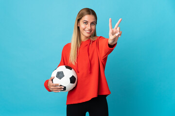 Young football player woman isolated on blue background smiling and showing victory sign