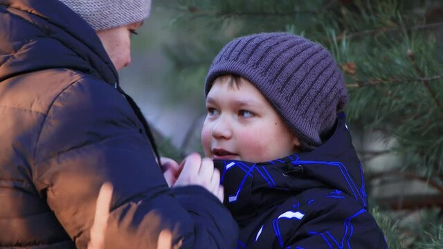 Close-up of happy mom and son caringly warm their hands to each other. Loving family outdoors in winter.People walk through the snow-covered forest in the evening at sunset.Beautiful natural landscape
