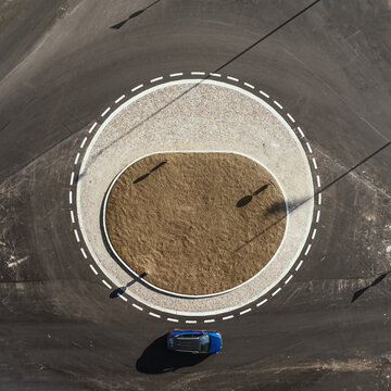 Aerial view of a blue car driving along a roundabout in Osnago, Lombardy, Italy.