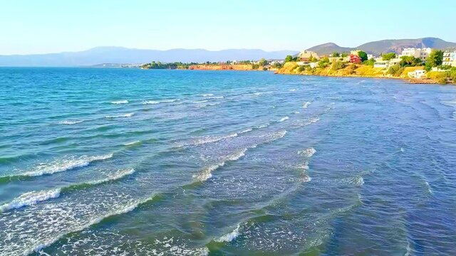 Aerial shot of waves rolling toward the coast and Chalcis, a beautiful town in Greece