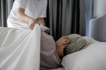 Asian senior woman is sleeping on a bed in bedroom,female caregiver cover senior patient with...