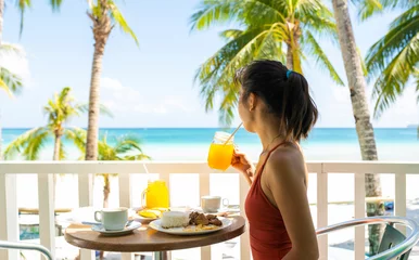 Photo sur Plexiglas Plage blanche de Boracay Une jeune fille en maillot de bain prend son petit déjeuner sur un balcon surplombant une belle plage de sable blanc baignée par une mer turquoise. Boracay, Philippines. Boracay est une petite île du centre des Philippines.
