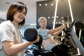 Asian woman working out with dumbbell,physical exercise by lifting weights,old elderly sitting on the spinning bicycle,exercise together,daily workouts in the gym,healthy lifestyle,health care concept
