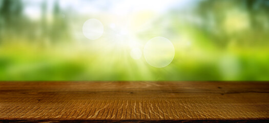 Blurred spring landscape with shining bokeh and empty wooden table. Sunny background with space for...