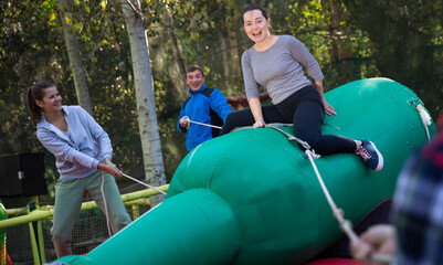 Friends having fun in outdoor amusement park, woman trying to stay in saddle on inflatable rodeo...