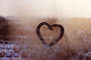 a romantic heart painted on a fogged window on a blurry street background