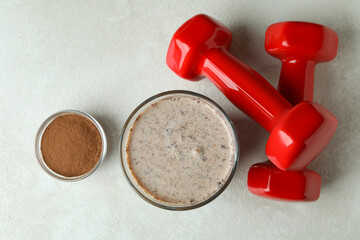 Chocolate milkshake, chocolate powder and dumbbells on white textured table