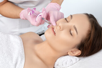 Obraz na płótnie Canvas Cosmetologist does injections for lips augmentation and anti wrinkle in the nasolabial folds of a beautiful woman. Women's cosmetology in the beauty salon.