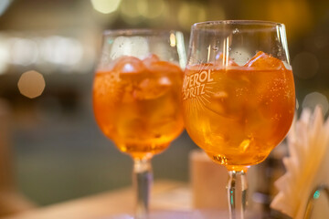 Two glasses of wine with  spritz stand on a wooden table in a cafe, in the rays of the setting sun. Italian alcoholic drink with oranges and ice. Close-up, selective focus,