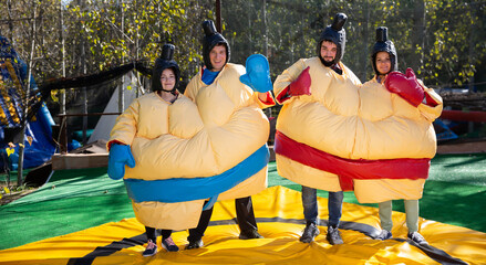 Portrait of happy excited men and women dressed as sumo wrestlers on inflatable arena - obrazy, fototapety, plakaty
