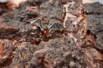 A brooch in the form of a bat made of bronze and amber against the background of birch slice