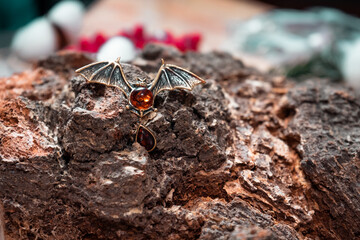 A brooch in the form of a bat made of bronze and amber against the background of birch slice