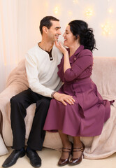 portrait of adult romantic couple sitting on a couch in home interior decorated with lights