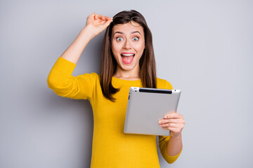 Portrait of lovely amazed cheerful girl holding in hands using tablet fast speed isolated over grey...