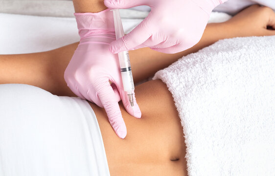 A doctor of aesthetic cosmetology makes lipolytic injections to burn body fat on a woman’s stomach and body. Female aesthetic cosmetology in a beauty salon.