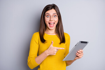 Portrait of lovely amazed cheerful girl holding in hands demonstrating tablet isolated over grey...