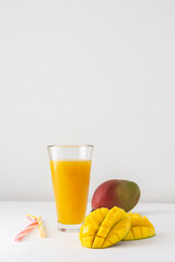 Mango juice in glasses with juice and a straw on a white background, chopped mango and whole, delicious healthy sweet natural drink