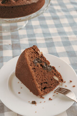 Chocolate pie on a white plate with a spoon on the blue checkered tablecloth. Vintage style. Selective focus