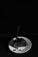 Chocolate pie on a white plate with a spoon with hard shadows on the black background. Black and white
