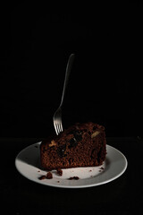 Chocolate pie on a white plate with a spoon with hard shadows on the black background. 