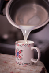 pouring boiled milk from the pot into the cup