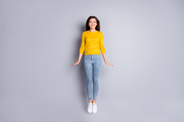 Full size photo of optimistic brunette nice lady jump wear yellow sweater jeans sneakers isolated on grey color background