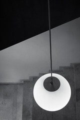 Round pendant lamp with a handrail at the top and stairs at the bottom. Vertical view. Black and white.