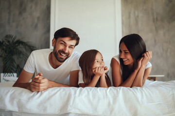 Excited family of three people resting on a bed