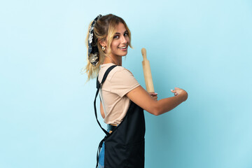 Young blonde Uruguayan cooking woman isolated on blue background pointing back