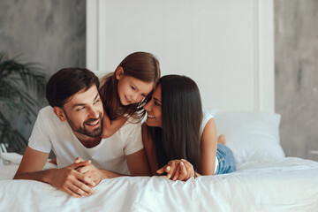 Adorable brunette child resting on a bed with mother and father