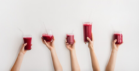 Multiple hands holding glasses with Purple beet and pomegranate fresh smoothie with glass straws, white background, copy space, wide composition. Detox, dieting, weight loss, healthy lifestyle concept