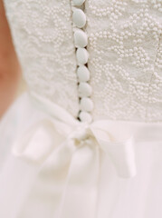 Fototapeta na wymiar White wedding dress close up. Elegant lace, bow and small fabric-covered buttons, bridal details macro.