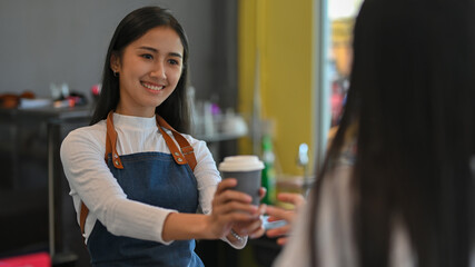 Portrait of female giving a cup of beverage to her customer in coffee shop