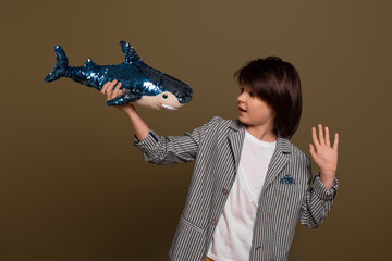Portrait of young boy posing with a toy shark in his hand in studio on green background. Casual style © Red Cristal