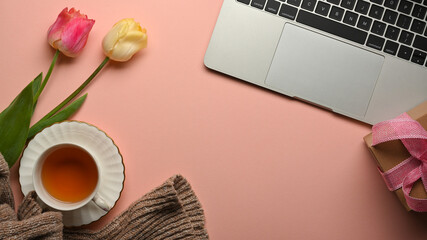 Top view of pink creative workspace with teacup, flowers, laptop and copy space