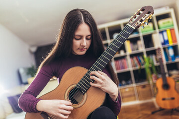 Pretty girl practicing some new sound on a guitar at home