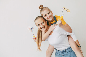 Beautiful and happy mom and daughter paint the walls in the apartment white, laugh and indulge